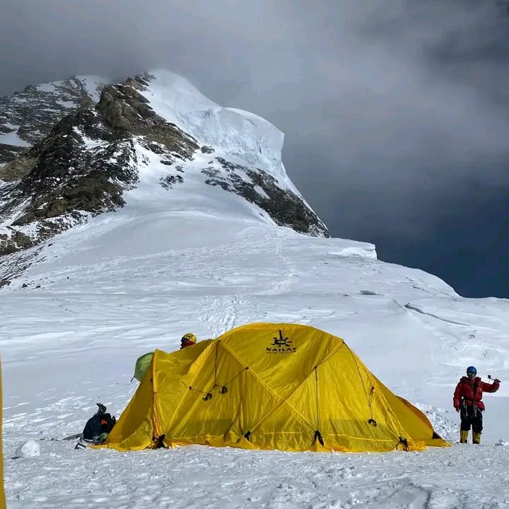 A yellow tent below a summit ridge under a stormy sky