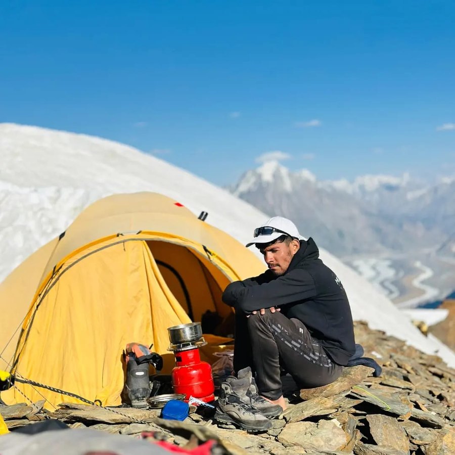 Sitting by a tent with a stove, mountains behind