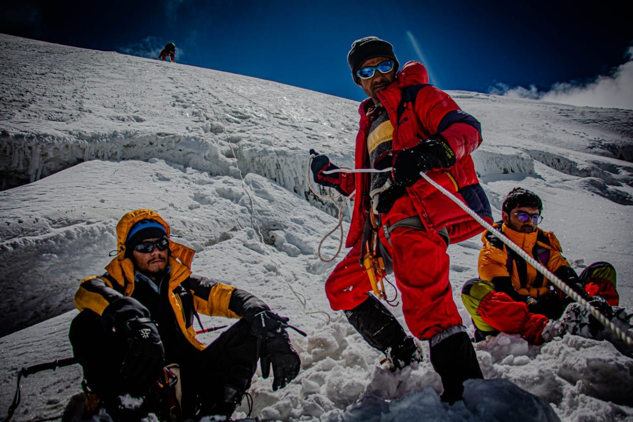 Three climbers resting on a fixed rope on a snow face