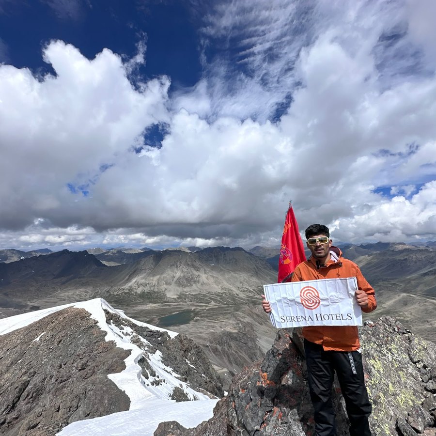 On a summit ridge with a sponsor flag and wide mountain view